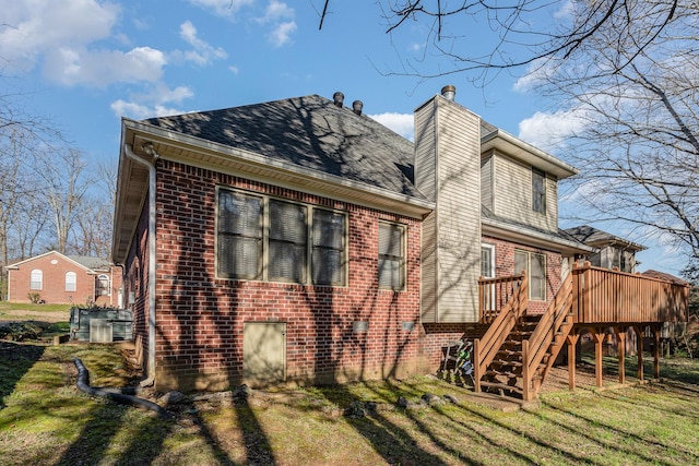 back of house featuring brick siding, stairway, a lawn, a chimney, and a deck