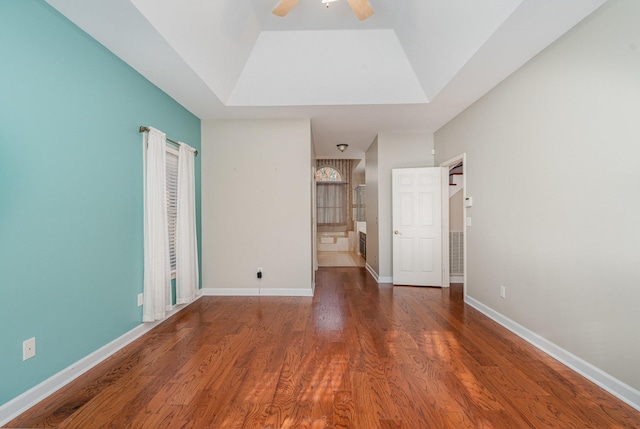 unfurnished bedroom with a ceiling fan, a tray ceiling, wood finished floors, connected bathroom, and baseboards