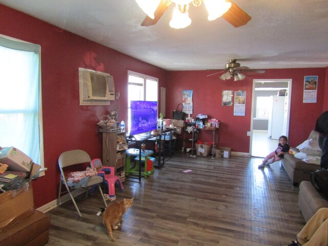 living room featuring baseboards, wood finished floors, a ceiling fan, and a wall unit AC