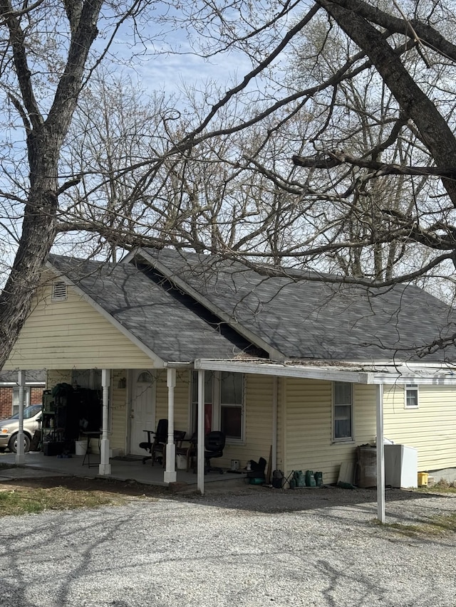 view of home's exterior featuring an attached carport, a shingled roof, and gravel driveway