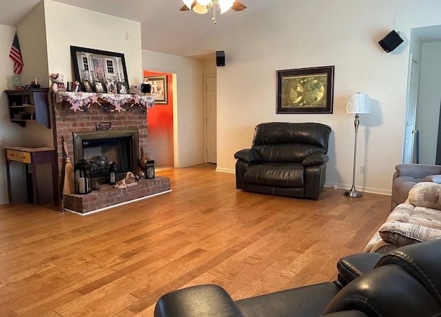 living area with lofted ceiling, light wood finished floors, baseboards, a brick fireplace, and ceiling fan