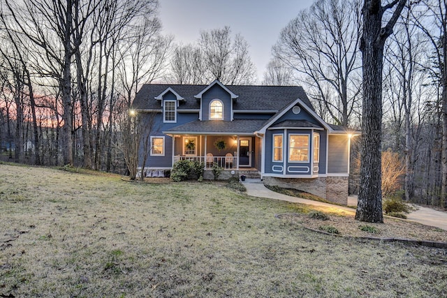 view of front of home with a yard, roof with shingles, and a porch