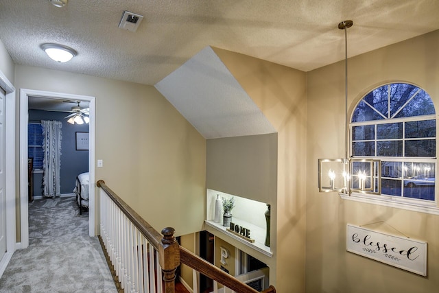 hall with an upstairs landing, visible vents, carpet flooring, and a textured ceiling