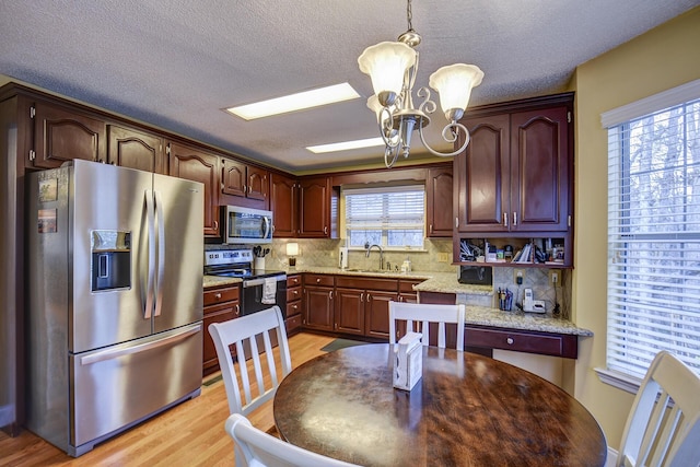 kitchen with decorative light fixtures, tasteful backsplash, stainless steel appliances, an inviting chandelier, and light wood finished floors