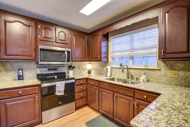 kitchen with light wood-type flooring, a sink, appliances with stainless steel finishes, decorative backsplash, and light stone countertops