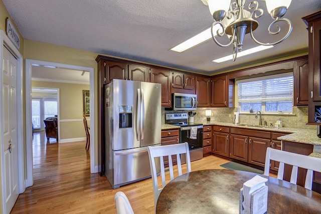 kitchen with a chandelier, light wood-style flooring, stainless steel appliances, and a sink