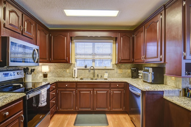 kitchen featuring light stone counters, light wood-type flooring, appliances with stainless steel finishes, and a sink