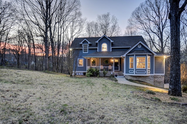 view of front of property featuring a yard, covered porch, and a shingled roof