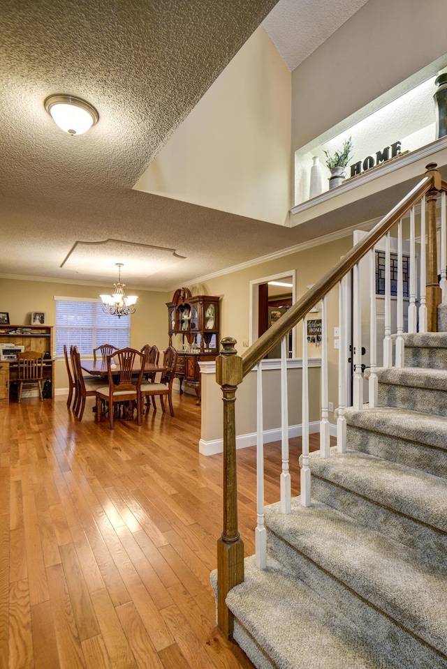 stairway featuring an inviting chandelier, crown molding, wood-type flooring, and a textured ceiling