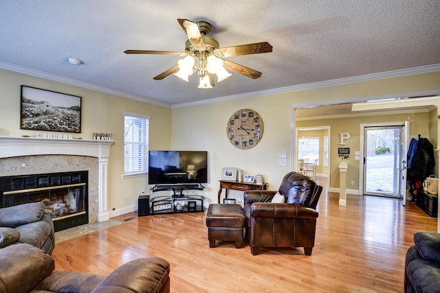 living room with ceiling fan, ornamental molding, a fireplace, light wood-style floors, and a textured ceiling