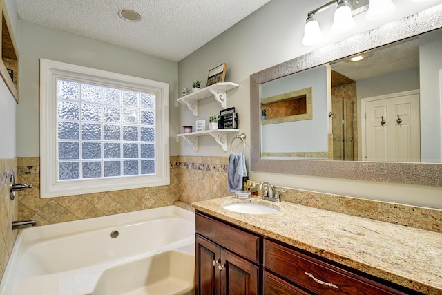 full bath featuring a stall shower, a textured ceiling, vanity, and a garden tub