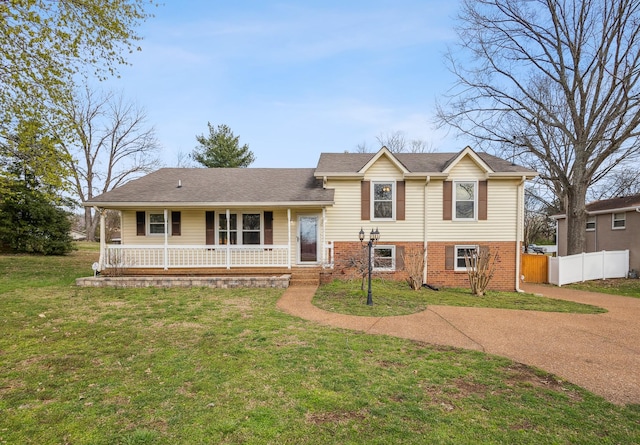 split level home with brick siding, a porch, a front lawn, and fence