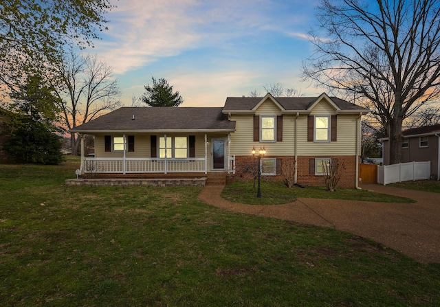 split level home featuring brick siding, a porch, fence, and a front lawn