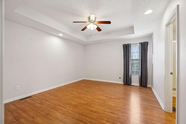 spare room with baseboards, light wood finished floors, a ceiling fan, and a raised ceiling
