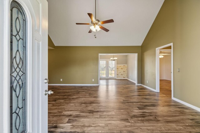 entryway with high vaulted ceiling, ceiling fan with notable chandelier, baseboards, and wood finished floors