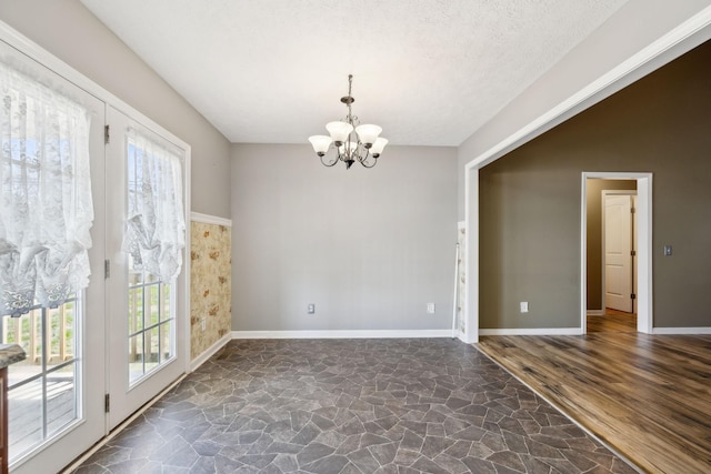 empty room featuring baseboards, a wealth of natural light, stone flooring, and a chandelier
