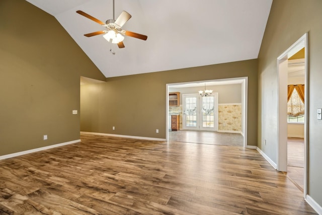 spare room with ceiling fan with notable chandelier, high vaulted ceiling, wood finished floors, and baseboards