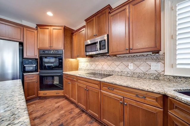 908 Plantation Blvd, Gallatin, TN 37066 - kitchen featuring light wood finished floors, backsplash, light stone countertops, brown cabinetry, and black appliances