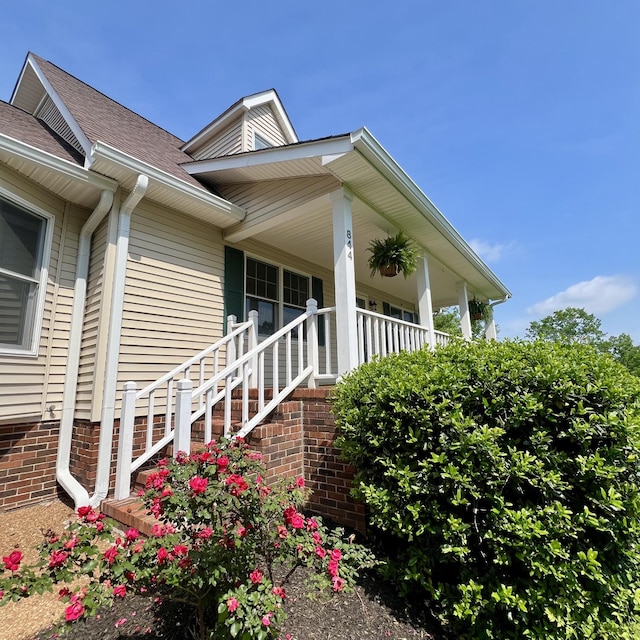 view of exterior entry featuring a porch and roof with shingles