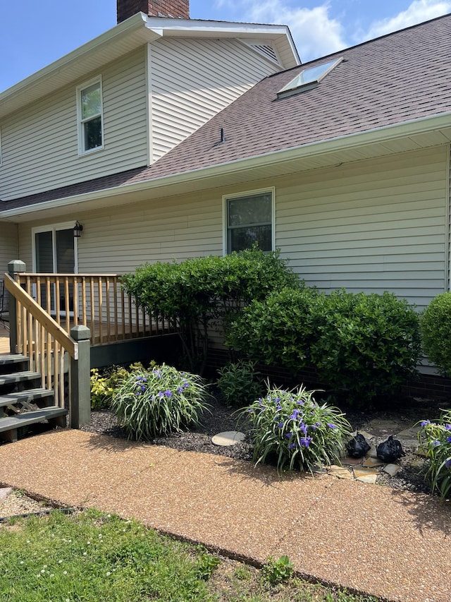 view of home's exterior featuring roof with shingles, a wooden deck, and a chimney