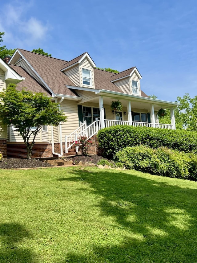 view of front of home featuring a shingled roof, covered porch, and a front yard