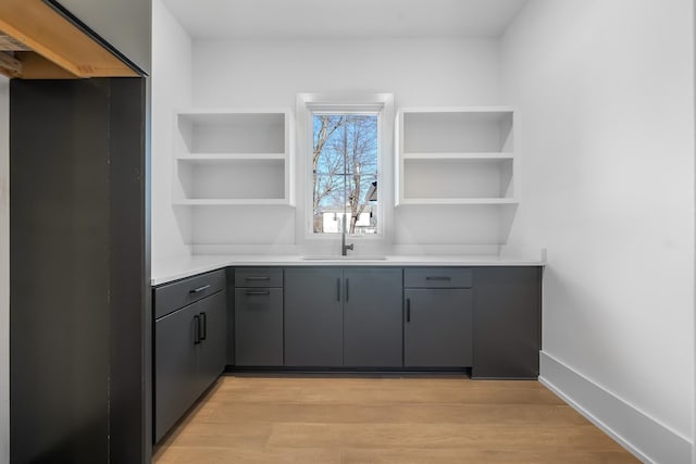 bar with a sink, baseboards, and light wood finished floors