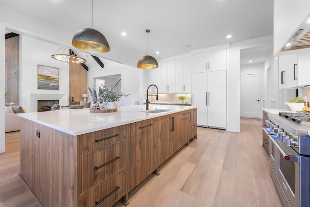 kitchen featuring a spacious island, wall chimney range hood, range with two ovens, modern cabinets, and a sink
