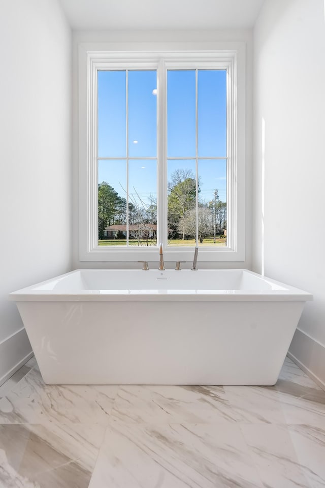 full bath with plenty of natural light, a soaking tub, and marble finish floor