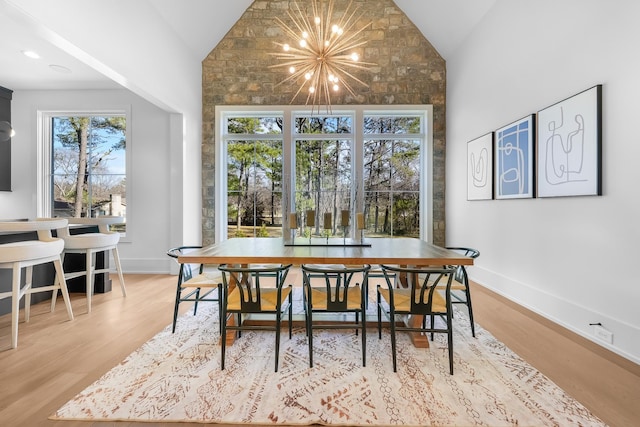 dining space with an inviting chandelier, wood finished floors, baseboards, and high vaulted ceiling