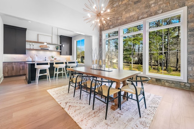 dining area featuring an inviting chandelier, light wood-style floors, and a towering ceiling