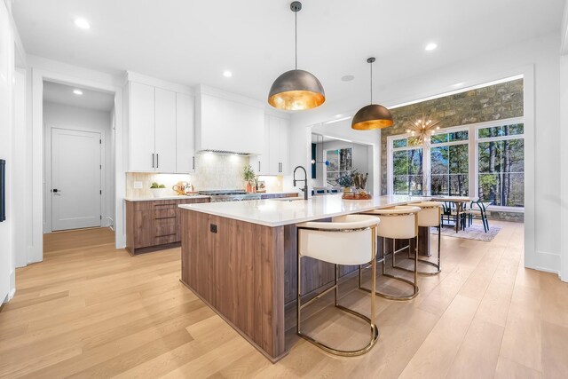 kitchen with a sink, a spacious island, light wood-style floors, white cabinets, and decorative backsplash