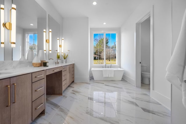 bathroom featuring a freestanding tub, marble finish floor, a sink, recessed lighting, and double vanity