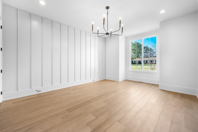 empty room featuring a notable chandelier, recessed lighting, light wood-type flooring, and baseboards