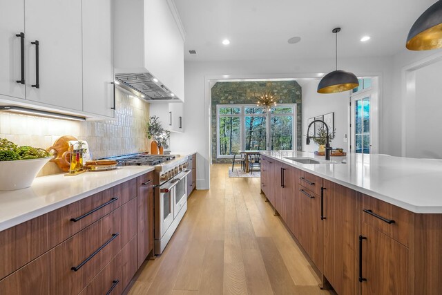 kitchen with range with two ovens, a sink, decorative backsplash, wall chimney exhaust hood, and modern cabinets