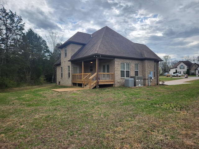 exterior space with a wooden deck, a shingled roof, a lawn, central AC, and brick siding