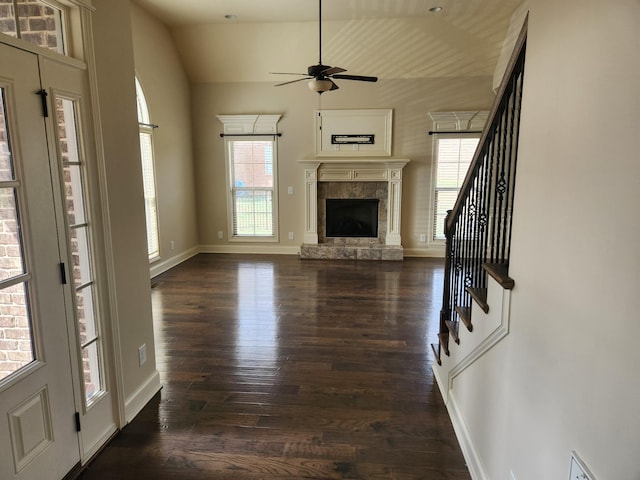 unfurnished living room featuring stairs, ceiling fan, a fireplace, baseboards, and dark wood-type flooring