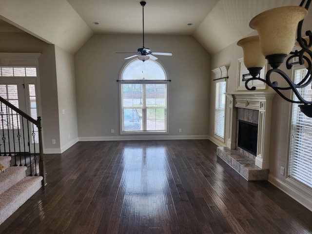 unfurnished living room featuring a tile fireplace, vaulted ceiling, stairway, a ceiling fan, and dark wood-type flooring