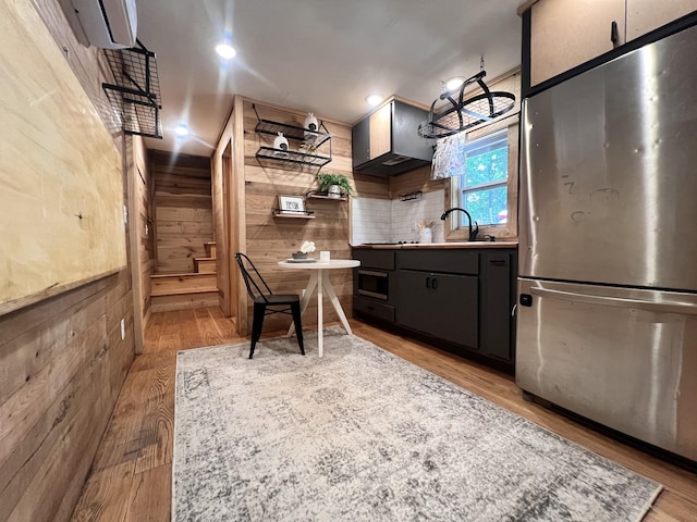 kitchen with freestanding refrigerator, decorative backsplash, wood walls, light wood-style floors, and a sink