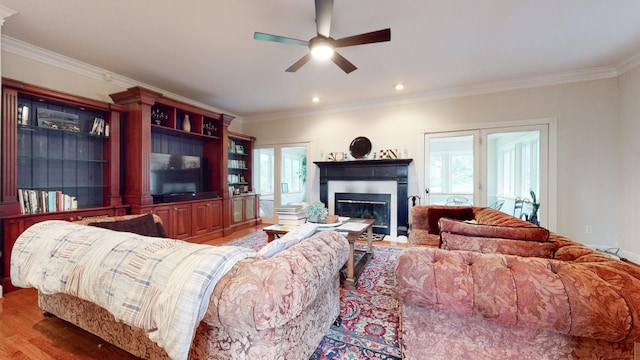 living area featuring a glass covered fireplace, ornamental molding, wood finished floors, and ceiling fan