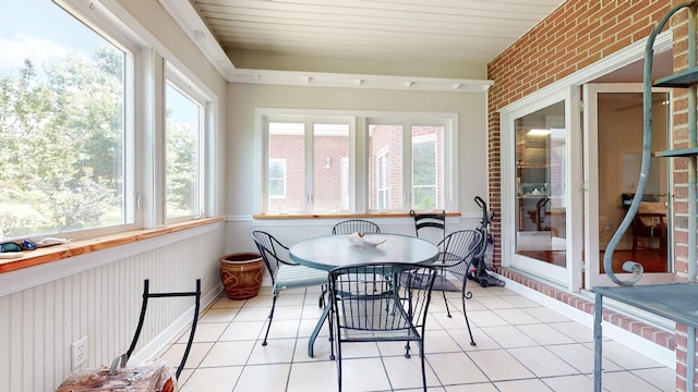 sunroom / solarium featuring tile patterned floors, outdoor dining area, and brick wall