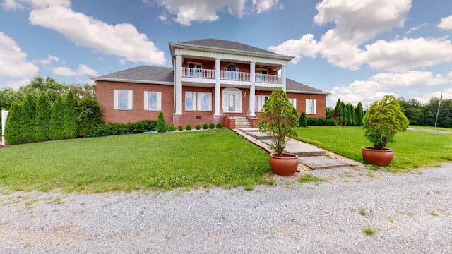 greek revival inspired property featuring a front yard, a balcony, and brick siding