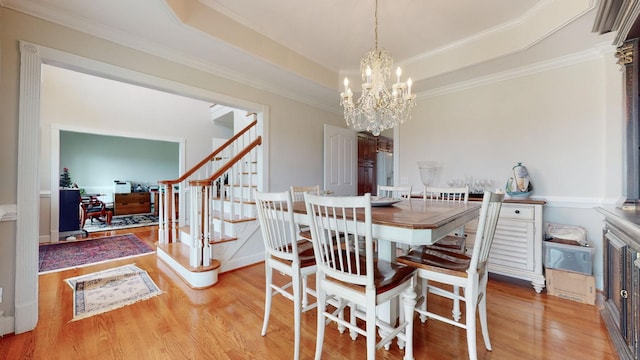 dining space featuring a notable chandelier, wood finished floors, crown molding, a raised ceiling, and stairs