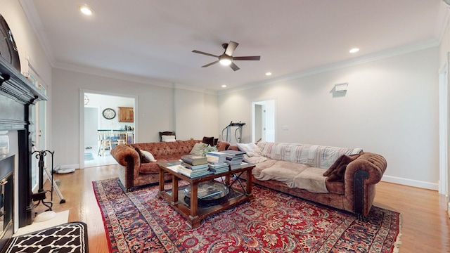 living room featuring a fireplace with flush hearth, a ceiling fan, recessed lighting, light wood-style floors, and crown molding
