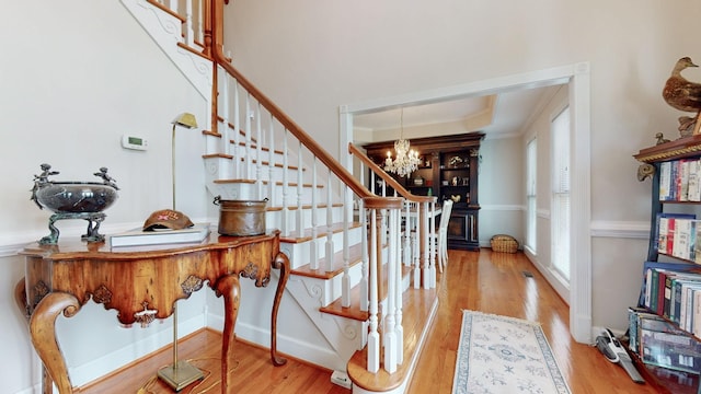 stairway featuring a tray ceiling, wood finished floors, crown molding, and a chandelier