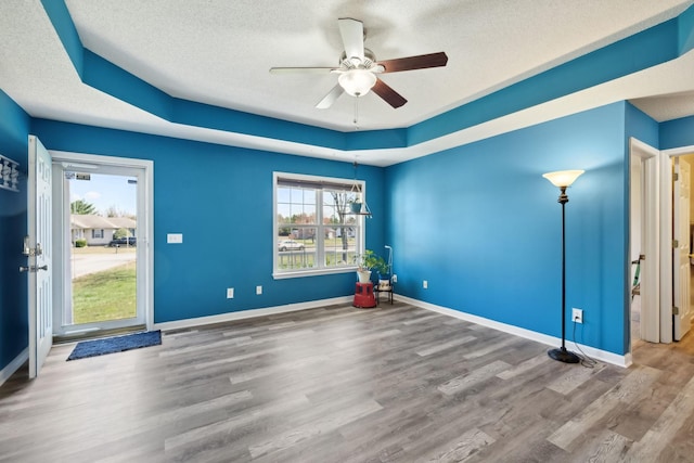 spare room featuring a raised ceiling, a ceiling fan, a textured ceiling, wood finished floors, and baseboards