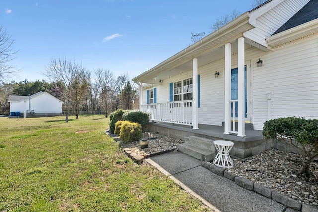 view of exterior entry with a yard, fence, and covered porch