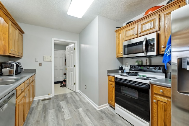 kitchen featuring baseboards, light wood finished floors, a sink, stainless steel appliances, and a textured ceiling