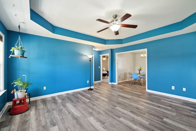 spare room with ceiling fan with notable chandelier, a raised ceiling, baseboards, and wood finished floors