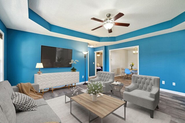 living room featuring baseboards, a raised ceiling, wood finished floors, and ceiling fan with notable chandelier