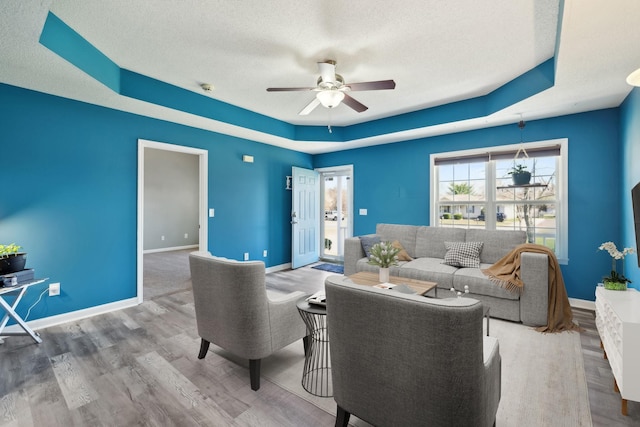 living area with a textured ceiling, wood finished floors, baseboards, and ceiling fan